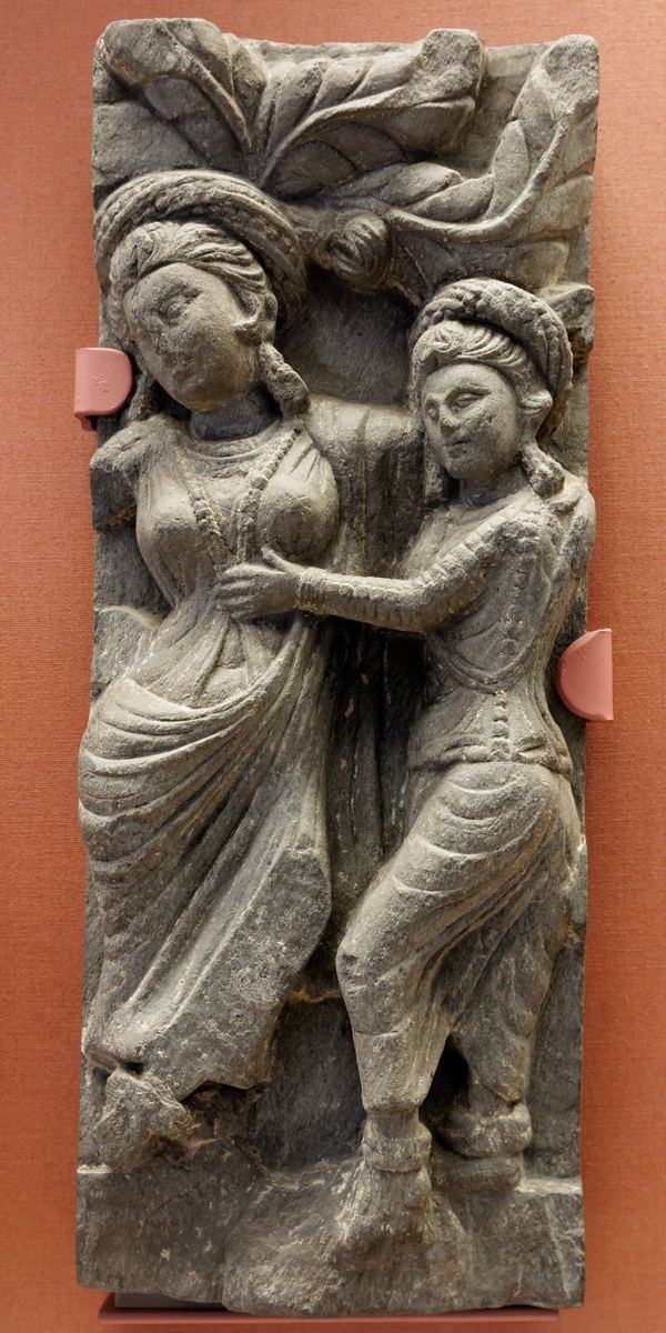 Steinrelief aus Gandhara: stehende Frau hält einen Ast, neben ihr kleine Figuren