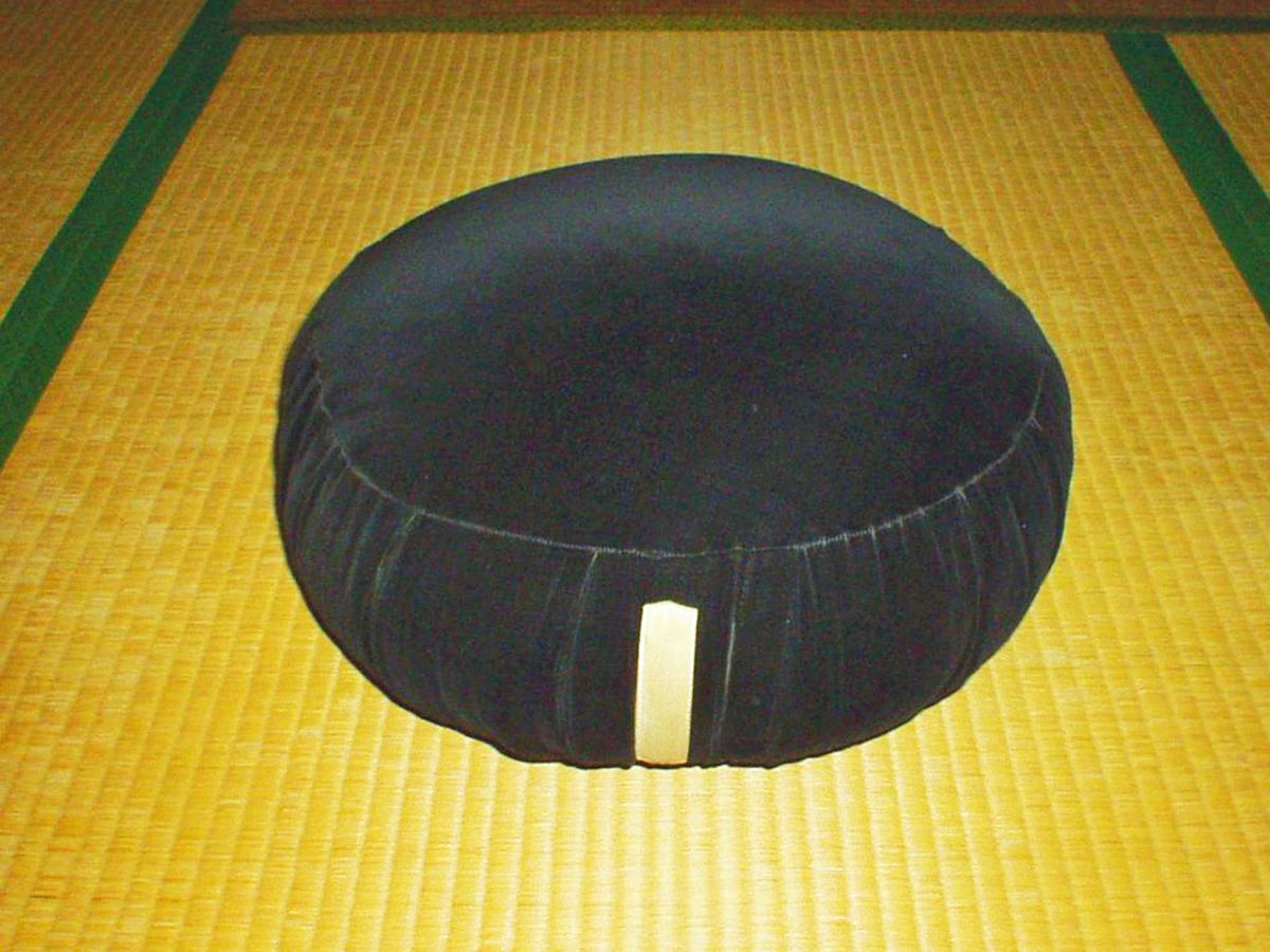 Rundes schwarzes Meditationskissen auf einer flachen Matte